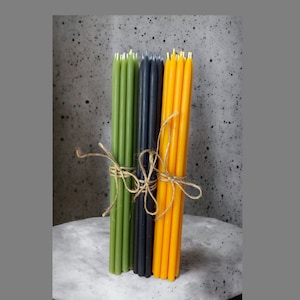 May include: A bundle of green, black, and yellow taper candles tied together with twine. The candles are all the same size and are arranged in a vertical stack.