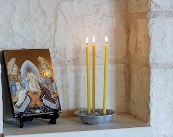 May include: A framed religious icon depicting Jesus Christ ascending to heaven, with angels and other figures surrounding him. Three yellow candles are burning in a small metal dish in front of the icon.