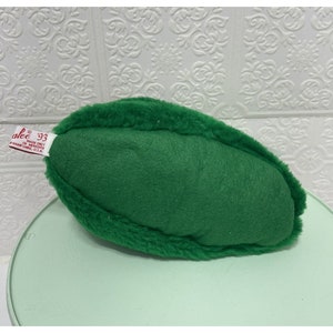 May include: A green plush pickle toy with a red label that reads "alee 93 MADE ONLY IN MEREDITH, NEW HAMPSHIRE, U.S.A."