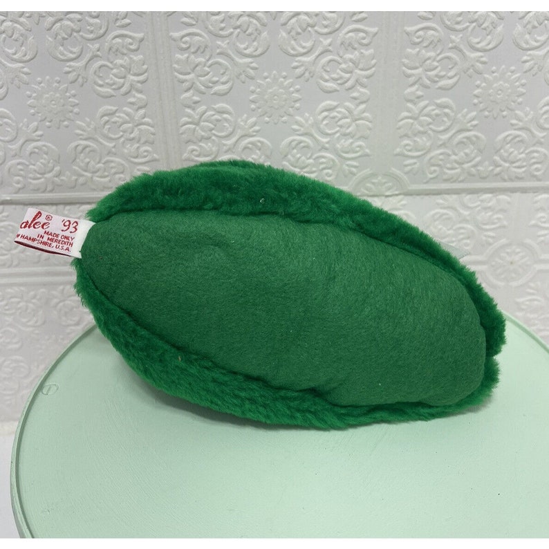 May include: A green plush pickle toy with a red label that reads "alee 93 MADE ONLY IN MEREDITH, NEW HAMPSHIRE, U.S.A."
