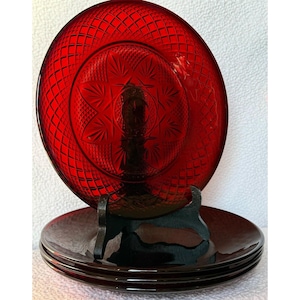 May include: Set of four red glass dinner plates with a diamond pattern and a starburst design in the centre.