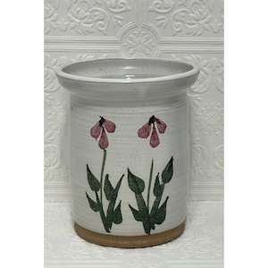 Puede incluir: Porta cubiertos de cerámica blanca con un borde marrón y dos flores rosas con tallos verdes pintados en la parte delantera.