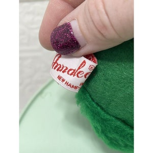 May include: Close-up of a green plush toy with a white label that reads "Annalee's New Hampshire".