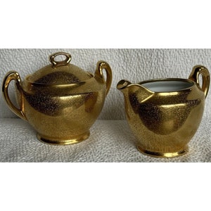 Puede incluir: Un juego de cremera y azucarero chapado en oro con un acabado moteado. La cremera y el azucarero tienen un interior blanco.