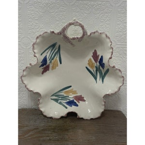 May include: White ceramic serving dish with a scalloped edge and a handle. The dish is decorated with a floral pattern of blue, yellow, and pink flowers.