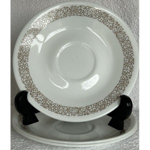 May include: Three white ceramic saucers with a brown floral design around the edge.