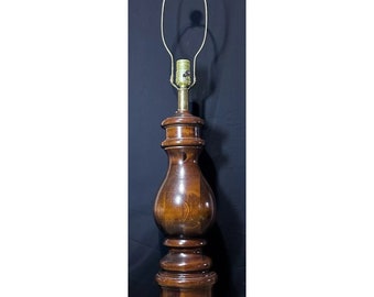 May include: A tall wooden lamp with a brown finish and a brass base. The lamp has a simple design with a round base and a bulbous middle section. The lampshade is missing.