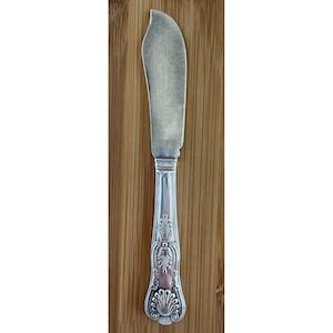 May include: Silver butter knife with a curved blade and ornate handle. The handle features a detailed floral and shell design with a pink accent. The knife is set against a wooden background.