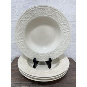 May include: Set of four white ceramic soup bowls with an embossed floral design. The bowls are stacked on top of each other.