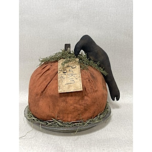 Könnte beinhalten: Ein orangefarbener Stoffkürbis mit einem Etikett "Pumpkin Pie". Eine schwarze Krähenfigur sitzt obenauf, mit dekorativem Grün. Der Kürbis steht auf einem Metallteller. Eine charmante Herbstdekoration.