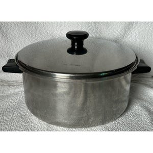 Puede incluir: Una olla de acero inoxidable con tapa y asa negras. La olla tiene un acabado brillante y es adecuada para cocinar en la estufa.