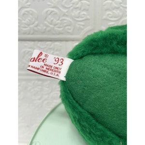 May include: Green plush avocado toy with a white tag that reads "alee '93 Made Only In Meredith, NH, U.S.A."