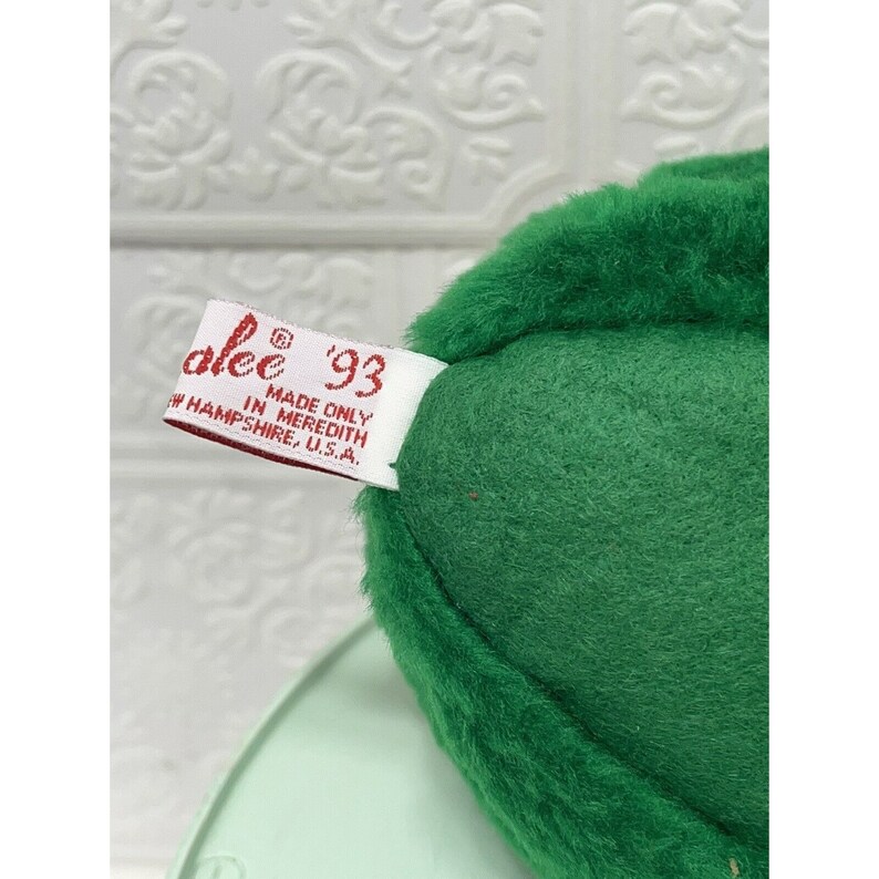 May include: Green plush avocado toy with a white tag that reads "alee '93 Made Only In Meredith, NH, U.S.A."