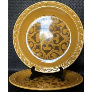 Könnte beinhalten: Zwei braune Keramik-Dinnerteller mit einem erhöhten Rand und einem braunen und goldenen geometrischen Muster.