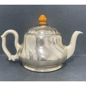 May include: A silver teapot with a white handle and a bright orange knob on the lid.