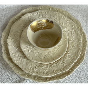 May include: A set of three white ceramic plates with an embossed oak leaf design. The plates are nested together and the smallest plate has a gold rim and a gold design in the center.