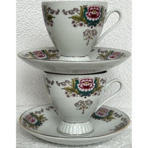 May include: Two white teacups and saucers with a floral design. The cups have a pink and green floral pattern with gold accents. The saucers have a matching floral design.