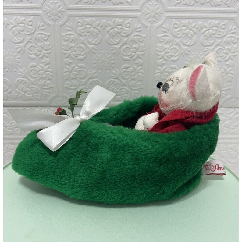 May include: A white plush mouse wearing a red coat is nestled in a green felt stocking with a white bow and holly sprig.