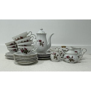 May include: A white porcelain tea set with a rose pattern. The set includes a teapot, creamer, sugar bowl, and six cups and saucers.