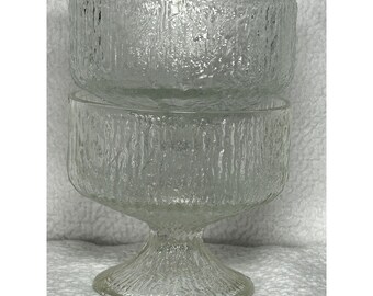 May include: Clear glass serving bowl with a textured, bark-like pattern. The bowl is elevated on a pedestal base, creating a layered effect. The glass has a frosted appearance, adding to its vintage aesthetic.