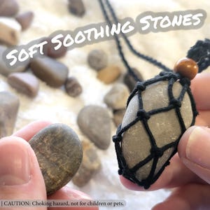 May include: A collection of smooth, gray stones, one held in a black net pendant. The text "SOFT SOOTHING STONES" is visible. The image also includes a warning about choking hazards.