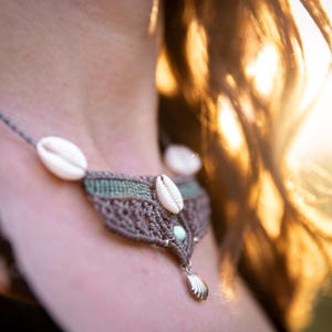 Könnte beinhalten: Nahaufnahme einer Frau, die eine Makramee-Halskette mit Muscheln und einem grünen Steinanhänger trägt. Die Halskette ist braun und hat ein zartes, filigranes Design.