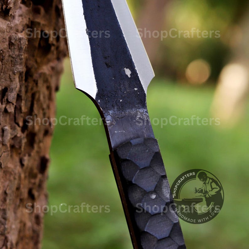 K&ouml;nnte beinhalten: Nahaufnahme eines handgefertigten Messers mit schwarzem Griff und silberner Klinge. Der Griff hat ein strukturiertes, geometrisches Muster. Die Klinge ist scharf und abgewinkelt. Der Text "ShopCrafters" ist sichtbar.