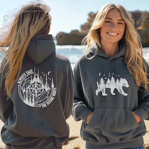 May include: Grey hooded sweatshirt with a white graphic design on the front and back. The front design features a bear walking through a forest with a moon and birds. The back design features a compass with the text "Always Take The Scenic Route".