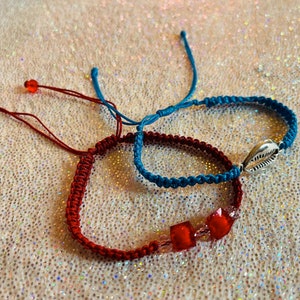 Puede incluir: Tres pulseras de la amistad, una roja con cuentas de vidrio rojas, una azul con un dije de concha de mar plateada y una azul con un dije de concha de mar plateada.