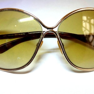 May include: Oversized sunglasses with a gold-tone frame and gradient yellow lenses. The arms are dark brown. The brand name "TOM FORD" is visible on the lens. These sunglasses offer a stylish, retro look.