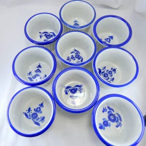 May include: Nine white ceramic ramekins with a blue floral design in the center and a blue rim. The ramekins are arranged in a circular pattern, perfect for serving individual portions of desserts or appetizers.