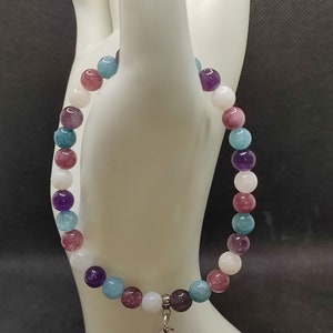 Peut inclure: Un bracelet composé de perles multicolores avec un charme argenté. Le bracelet présente des perles dans des tons de bleu, violet, rose et blanc.