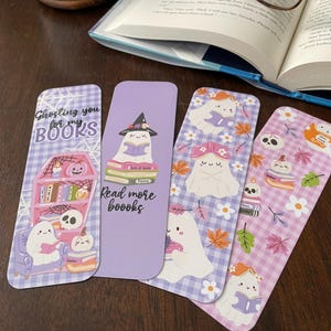 May include: Four decorative bookmarks with ghost illustrations. One bookmark has the text "Ghosting you for my books". Another says "Read more boooks". The bookmarks feature ghosts reading books, pumpkins, and floral designs.