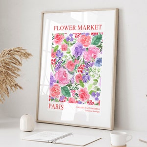 May include: A framed watercolor print featuring a floral design with pink, purple, and red roses, along with other flowers and greenery. The words "FLOWER MARKET PARIS" are printed in red at the top and bottom of the print. The print is displayed on a white surface.