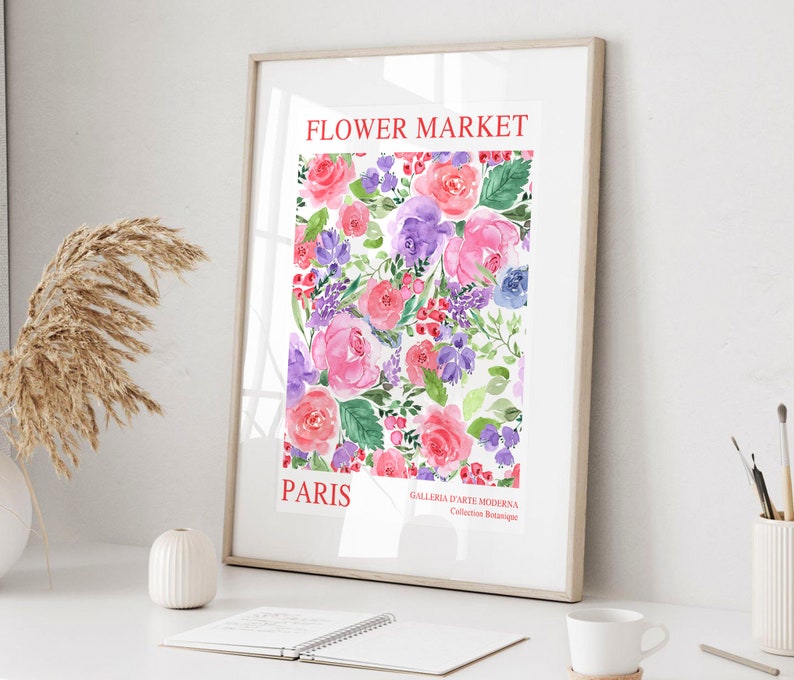 May include: A framed watercolor print featuring a floral design with pink, purple, and red roses, along with other flowers and greenery. The words "FLOWER MARKET PARIS" are printed in red at the top and bottom of the print. The print is displayed on a white surface.