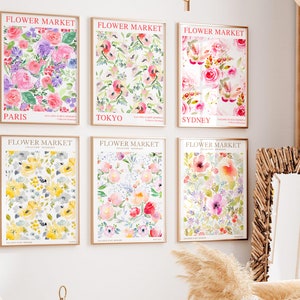 May include: Six framed floral art prints. Each print features a watercolor floral design with the words "FLOWER MARKET" at the top and a city name at the bottom. The prints showcase various flowers in shades of pink, purple, yellow, and red.