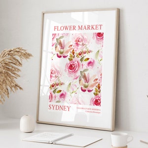 May include: A framed art print featuring a watercolor floral pattern of pink roses and foliage. The print includes the text "FLOWER MARKET SYDNEY" in red, with additional text at the bottom. The artwork is displayed on a white surface.