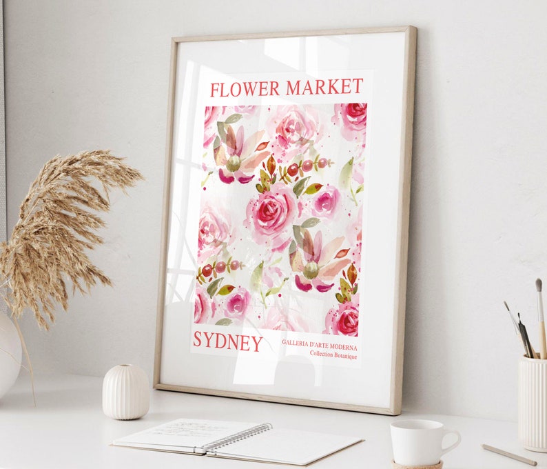 May include: A framed art print featuring a watercolor floral pattern of pink roses and foliage. The print includes the text "FLOWER MARKET SYDNEY" in red, with additional text at the bottom. The artwork is displayed on a white surface.