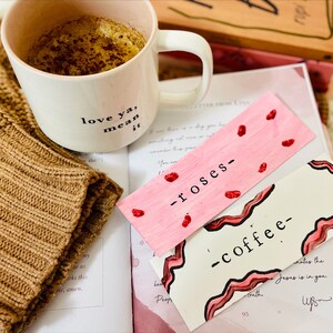May include: Two handmade bookmarks with pink and red accents. One bookmark says "roses" and the other says "coffee".