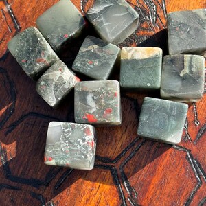 May include: A collection of ten green, black, and red tumbled stones with a speckled pattern. The stones are cube-shaped and have a polished finish.