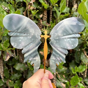 May include: A decorative butterfly figurine with a grey and white painted finish. The butterfly has a gold body and is mounted on a wooden stand.