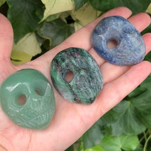 May include: Three smooth, polished stones with holes drilled through the centre. The stones are green, blue, and a mix of green and pink.