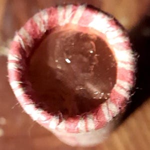 May include: A roll of pennies, viewed from above, with a red and white striped paper wrapper. The coins inside are visible, with a profile of a person on the penny.