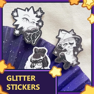 May include: Three die-cut glitter stickers featuring black and white anime-style character illustrations. The stickers display a spiky-haired figure, a character with glasses and dark hair, and a figure wearing a pointed hat, all accented with sparkles.