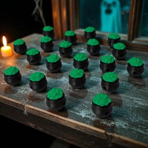 May include: A collection of small, black cauldron-shaped objects, each topped with bright green, textured material. The cauldrons are arranged on a weathered wooden surface, with a lit candle and a ghostly figure in the background, creating a Halloween theme.