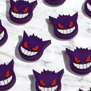 May include: Multiple purple and white 3D printed Ghost Pokemon figures with red eyes.