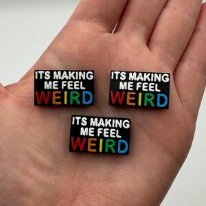 May include: Three black rubber shoe charms with the text "ITS MAKING ME FEEL WEIRD" in white letters with rainbow colored outlines.