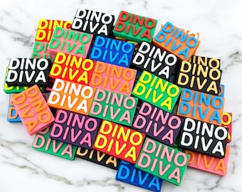 May include: A collection of colorful rectangular charms with the text "DINO DIVA" in various colors. The charms are in shades of pink, orange, green, blue, and black, with the text in contrasting colors.