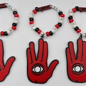 May include: Three red beaded bracelets with black and white beads. Each bracelet has a charm attached to it, a red hand with a black eye in the palm. The bracelets have the text "REZZ CULT" on them.