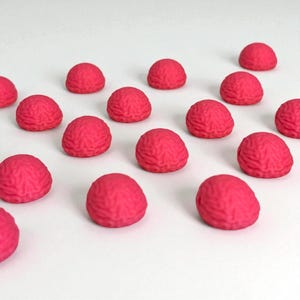 May include: A collection of small, brain-shaped objects in a vibrant shade of pink. The objects are arranged on a white surface, with a textured surface that mimics the appearance of a human brain. The overall effect is playful and eye-catching.